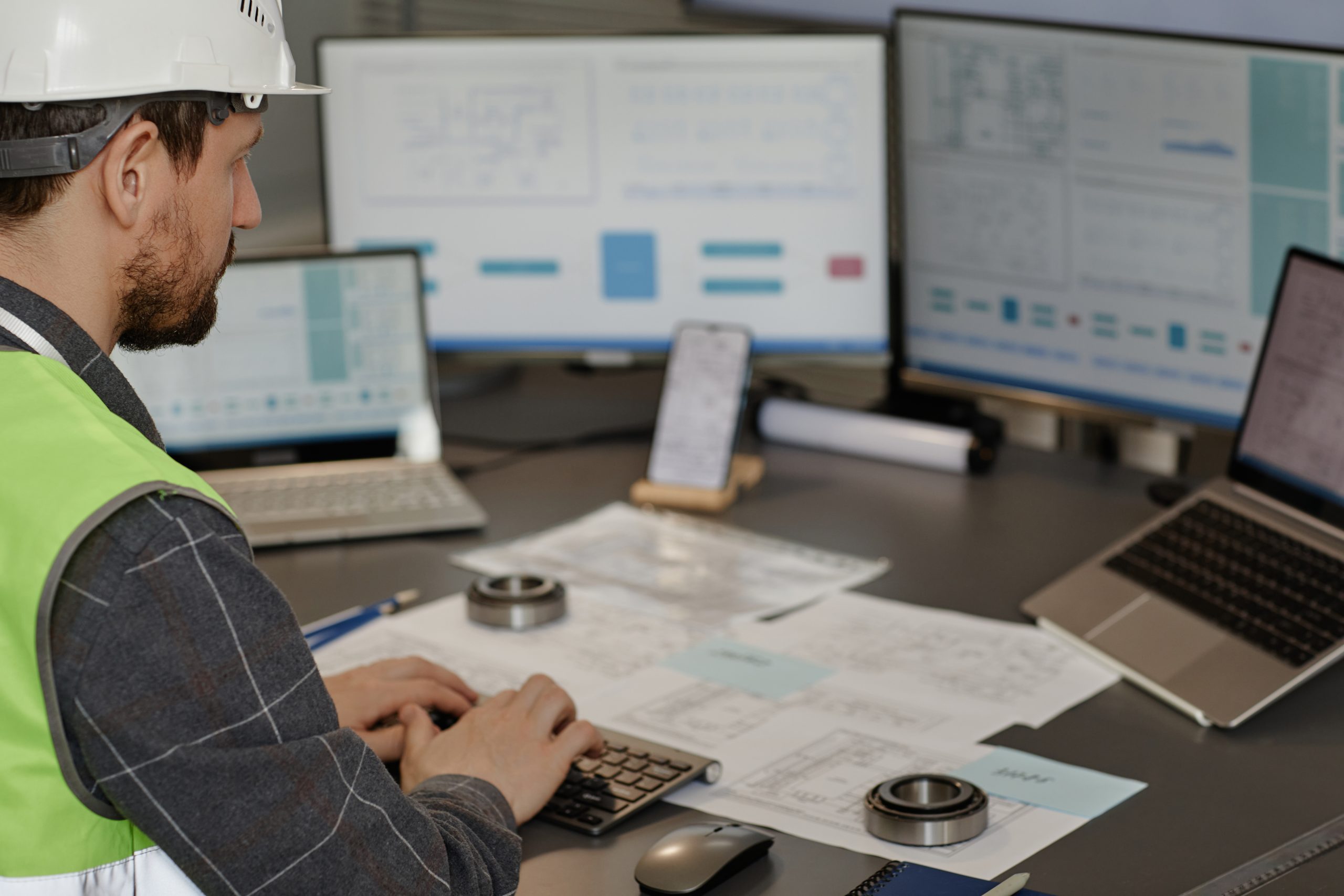 Side view of male engineer wearing hardhat at workplace in office and using computer designing blueprints, copy space